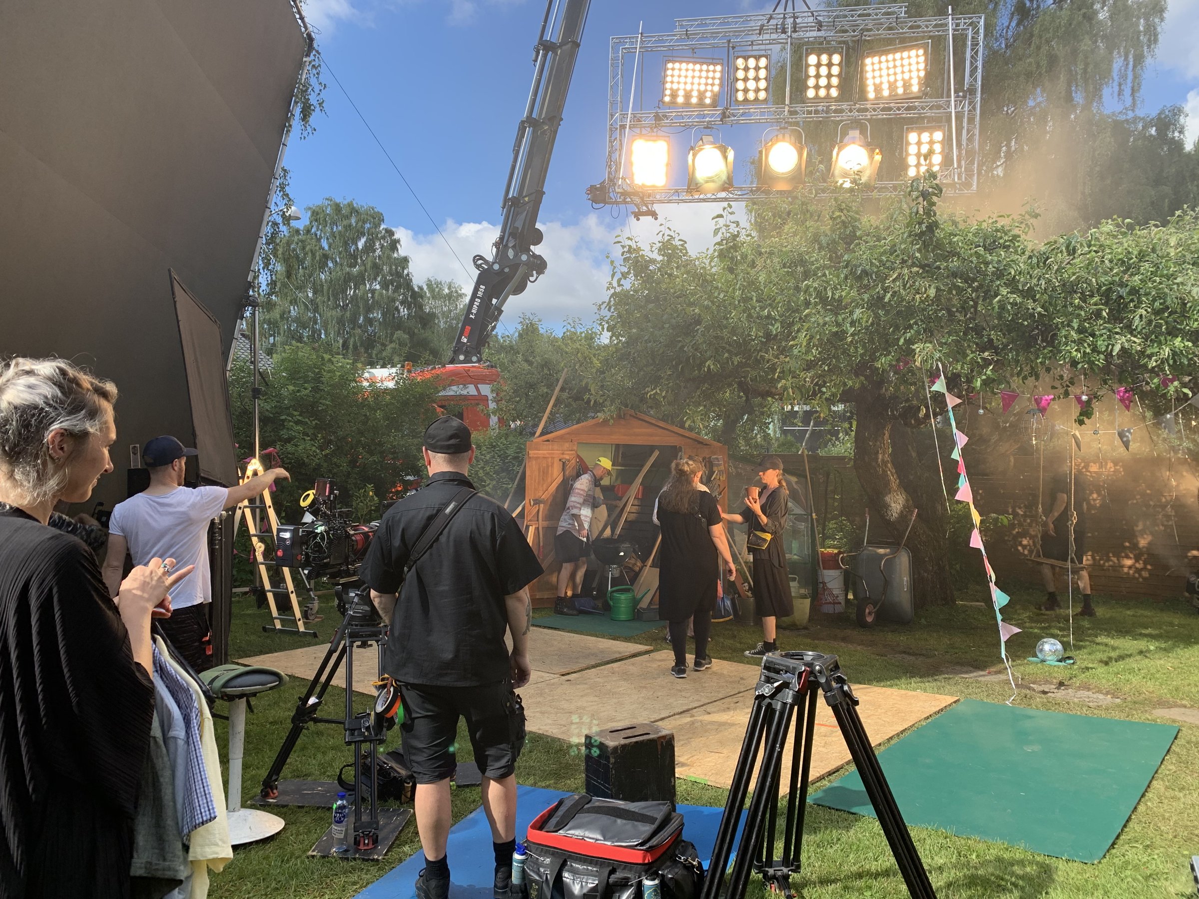 Film crew on location: crane, lighting rig and camera team on a summer set